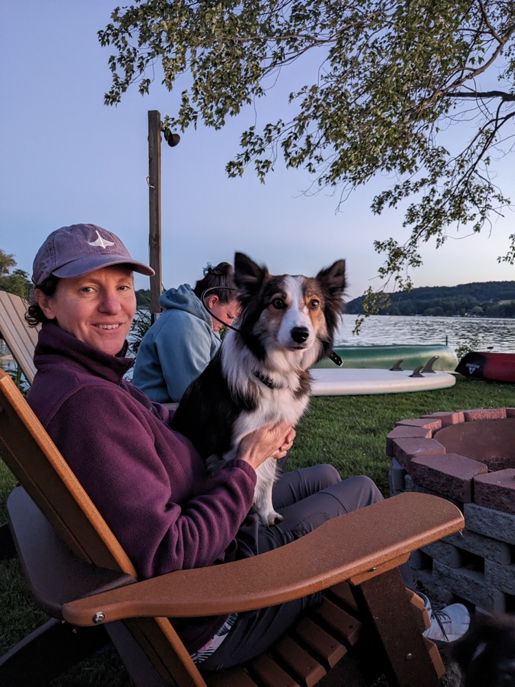 Tara, the founder, sitting outdoors at dusk with a tricolor Australian Shepherd on her lap.
